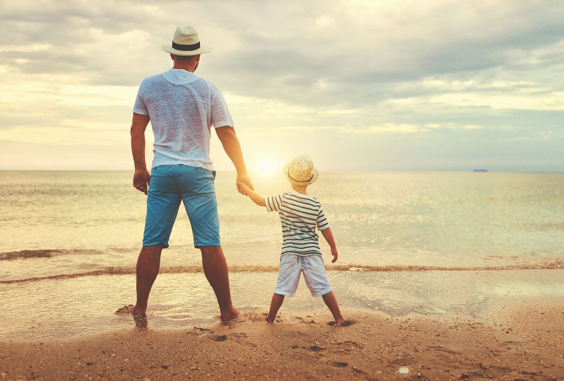 A father holds the hand of their son as they watch the setting sun on a shore. Learn how a christian counselor in Hillsboro, OR can offer support with child counseling in Clackamas, OR and other services including online therapy in Portland, OR.