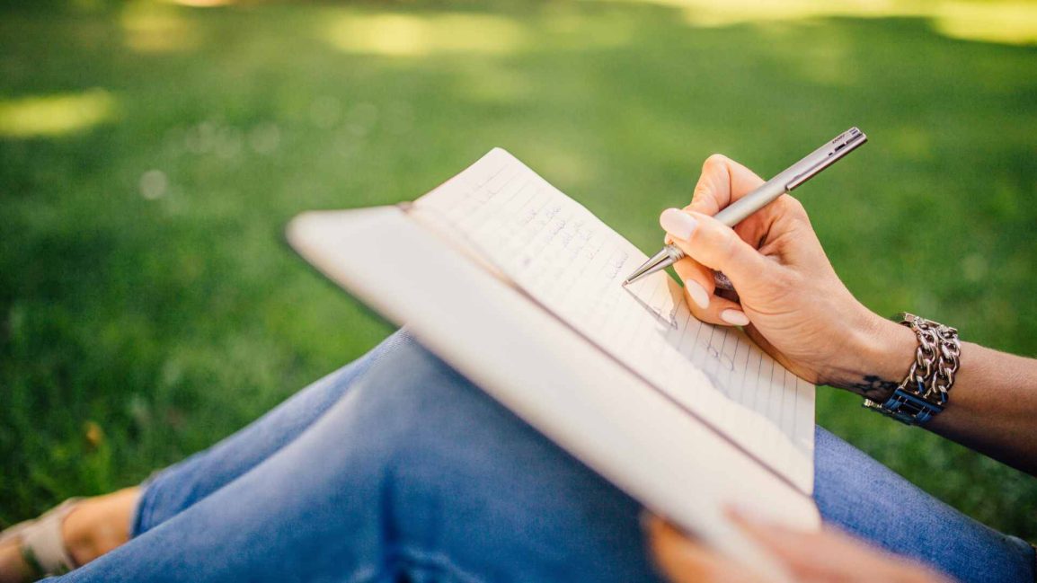 Woman sitting in the grass writing in her journal. Getting your anxious thoughts more in control with CBT therapy in Clackamas, OR can help! Meet with an expert Christian counselor here.